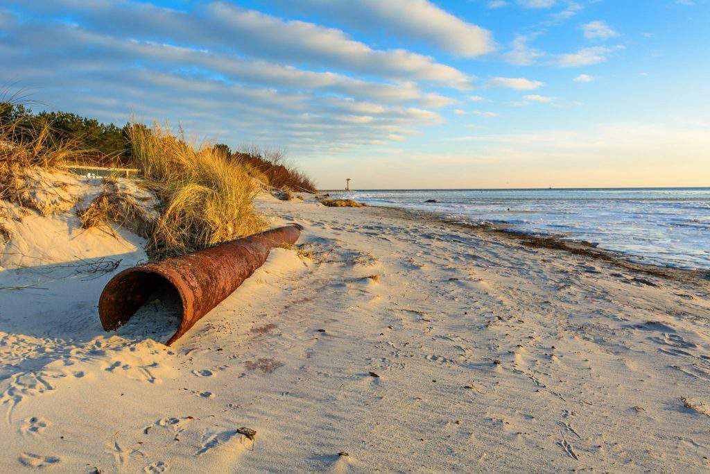 Big old rusty pipe on the sandy beach in warm light. Hel Peninsula. Poland