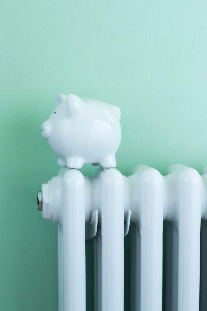 Piggy Bank Balanced On Radiator To Illustrate Energy Costs