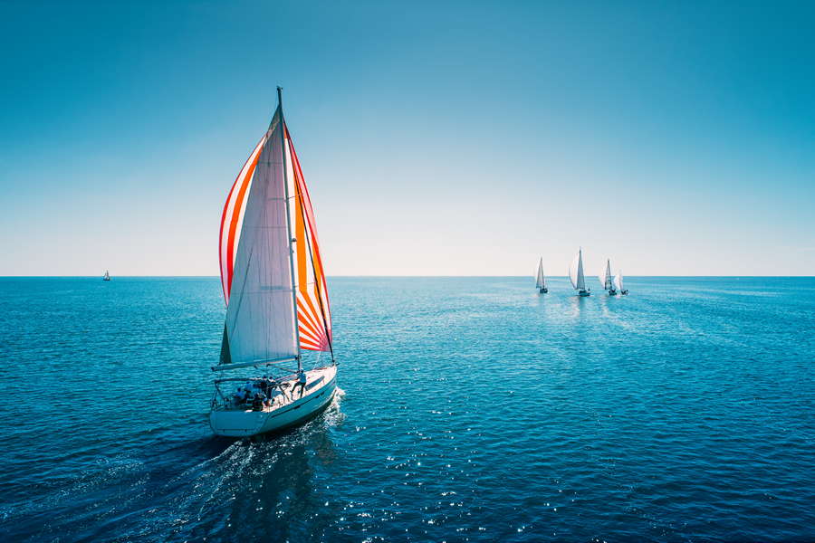 Regatta sailing ship yachts with white sails at opened sea. Aerial view of sailboat in windy condition.